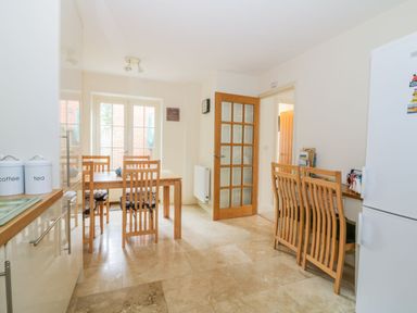 A dining area with a wooden table and six chairs near glass doors and a white refrigerator at 26 Burtons Mill in Stalham