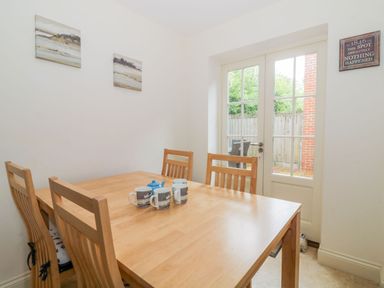 A dining area with a wooden table and four chairs near glass doors leading outside at 26 Burtons Mill in Stalham