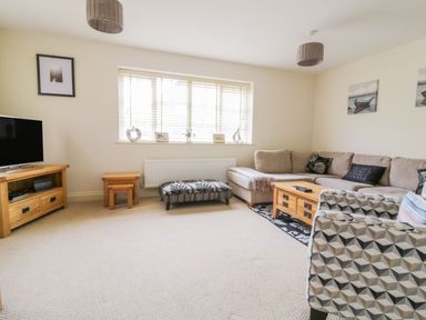 A living room with a beige sectional sofa a wooden coffee table patterned armchair and a television on a wooden stand at 26 Burtons Mill in Stalham