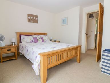 A bedroom with a wooden bed and floral bedding two bedside tables with lamps and an open door at 26 Burtons Mill in Stalham