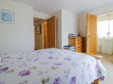 A bedroom with a floral bedspread a wooden dresser two open doors and a window at 26 Burtons Mill in Stalham