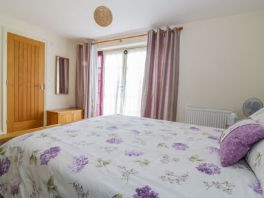 A bedroom with a floral bedspread a wooden door and a window with curtains at 26 Burtons Mill in Stalham