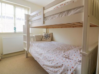 A bedroom with a white bunk bed and a window with blinds at 26 Burtons Mill in Stalham