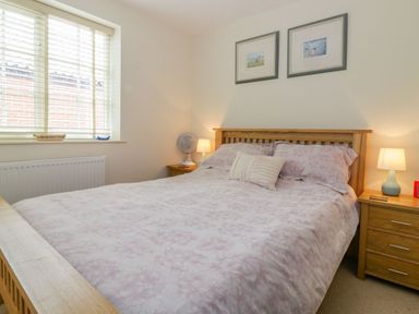 A bedroom with a bed with patterned bedding two bedside tables with lamps and framed pictures on the wall at 26 Burtons Mill in Stalham