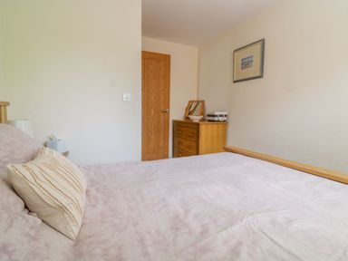 A bedroom with a bed pillow a wooden door a wooden chest of drawers a framed picture and a table lamp at 26 Burtons Mill in Stalham