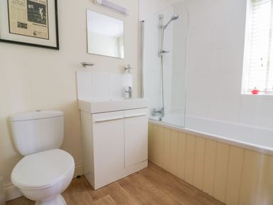 A bathroom with a toilet sink cabinet bath with shower and window at 26 Burtons Mill in Stalham