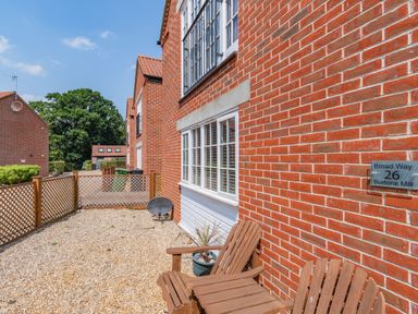 A gravel outdoor area with two wooden chairs and a potted plant outside a red brick house at 26 Burtons Mill in Stalham