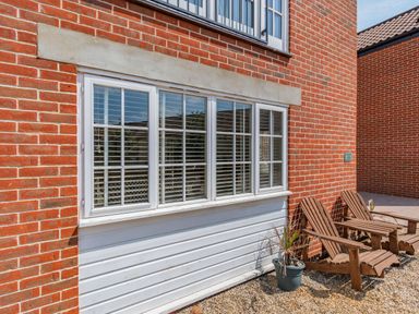 A brick exterior wall with a white framed window wooden chairs and a potted plant at 26 Burtons Mill in Stalham