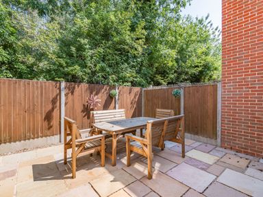 An outdoor patio with wooden table and chairs surrounded by wooden fencing and trees at 26 Burtons Mill in Stalham