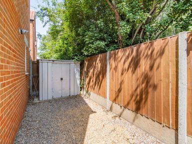 A small gravel yard with a white metal shed next to a brick building and wooden fence at 26 Burtons Mill in Stalham
