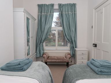 A bedroom with two twin beds with folded towels on top a white wardrobe with mirror blue curtains and a small bench at 202 Salisbury Terrace in York