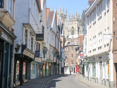 A narrow street lined with shops and historic buildings with a cathedral in the background in York