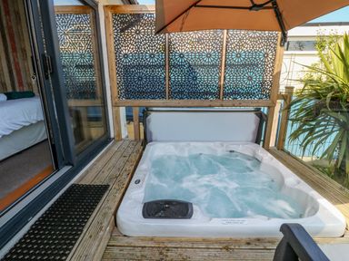 A bubbling outdoor hot tub on a wooden deck with a sliding glass door leading to a bedroom with a bed at Daisy Cottage in Benllech