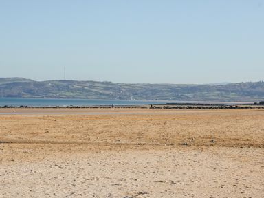 A sandy beach with a rocky barrier and hills in the background at Daisy Cottage in Benllech