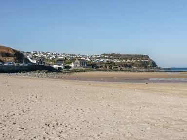 A sandy beach with a rocky shoreline and houses on a hill under a clear sky