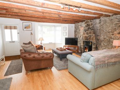 A living room with leather and fabric sofas a stone fireplace a television and a bay window at Arwel in Nefyn