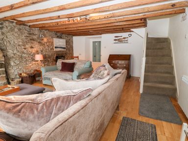 A living room with sofas a lamp and a wooden chest of drawers near carpeted stairs at Arwel in Nefyn
