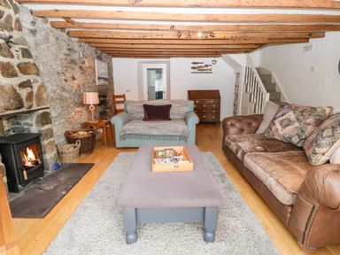 A living room with wood beams stone wall fireplace sofas and a central ottoman at Arwel in Nefyn