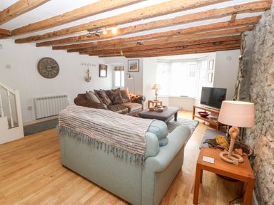 A living room with wooden beams on the ceiling stone wall two sofas a television and wooden furniture at Arwel in Nefyn