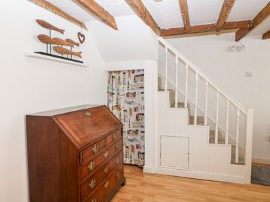 A wooden chest of drawers next to stairs with white railing and wooden beams on ceiling at Arwel in Nefyn