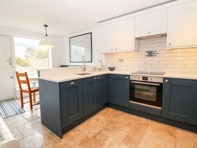 A kitchen with blue lower cabinets and white upper cabinets with a built-in oven and sink at Arwel in Nefyn