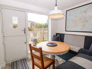A dining area with a round wooden table a wooden chair a corner bench with cushions a hanging light a striped rug and a framed map on the wall at Arwel in Nefyn