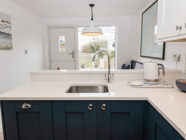 A kitchen with a sink, faucet, kettle on a tray, and a door leading outside at Arwel in Nefyn