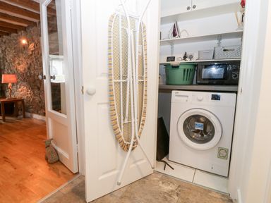 A laundry area with a washing machine, microwave, ironing board on door and laundry basket at Arwel in Nefyn