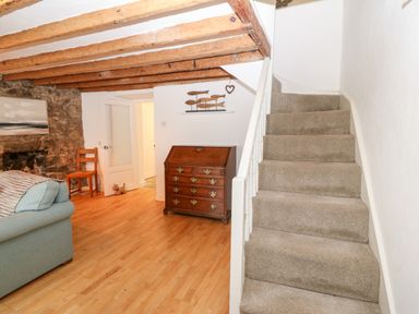 A room with wooden beams on the ceiling a staircase with carpet a wooden chest of drawers a wooden chair and a sofa at Arwel in Nefyn