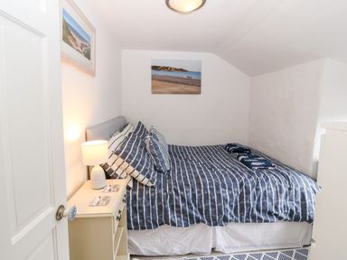 A bedroom with a bed covered in blue and white striped bedding a bedside table with a lamp and two framed beach photographs on the walls at Arwel in Nefyn