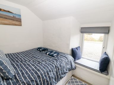 A small bedroom with a bed covered in striped bedding and a window seat with cushions at Arwel in Nefyn