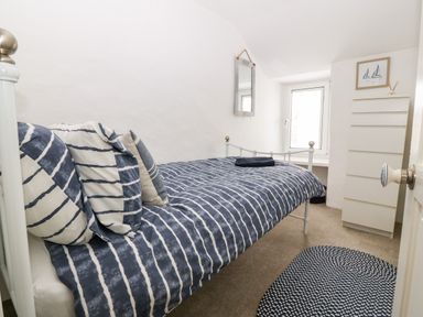 A bedroom with a bed covered in striped bedding pillows a tall white dresser a window a wall mirror and a patterned rug at Arwel in Nefyn