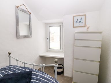 A bedroom corner with a bed, a tall white dresser, a mirror on the wall, a small window, and a framed picture at Arwel in Nefyn