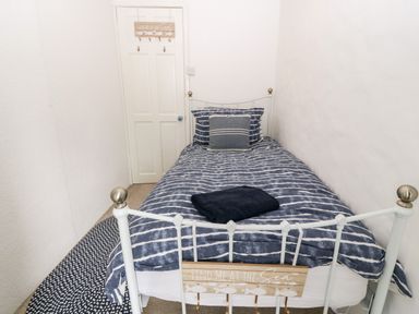 A small bedroom with a single bed with striped bedding and a pillow a wooden sign with hooks that says find me at the sea on the bed frame and a door with a matching wooden sign at Arwel in Nefyn