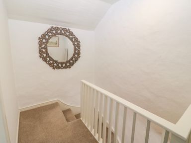 A staircase with beige carpet and white walls with a decorative round mirror at Arwel in Nefyn
