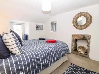 A bedroom with a bed covered with striped bedding towels on the bed a mirror above a stone fireplace at Arwel in Nefyn