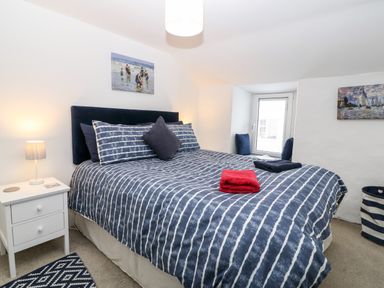 A bedroom with a bed with striped bedding bedside table with lamp window with cushions and paintings at Arwel in Nefyn