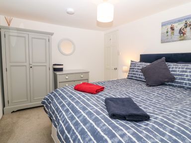 A bedroom with a bed dressed in blue striped bedding and towels on it with a gray wardrobe and dresser and a round mirror on the wall at Arwel in Nefyn