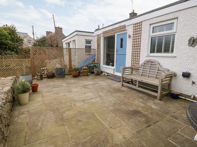 A paved outdoor patio area with a wooden bench pots with plants and a blue door at Arwel in Nefyn