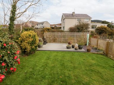 A backyard with a grassy lawn a wooden deck with potted plants and a wooden fence at Arwel in Nefyn