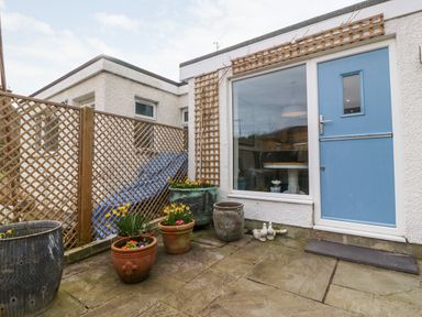 A small patio with flower pots and a blue door at Arwel in Nefyn