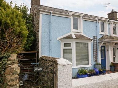 Exterior of a blue house with a bay window and blue front door with potted plants outside at Arwel in Nefyn