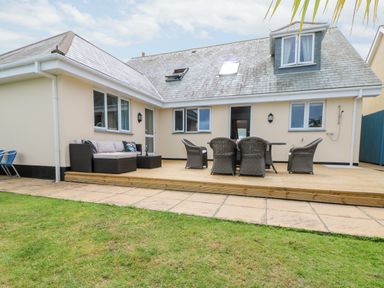 An outdoor patio area with wicker chairs and a sofa on a wooden deck attached to a beige house at Trevose House in Crantock