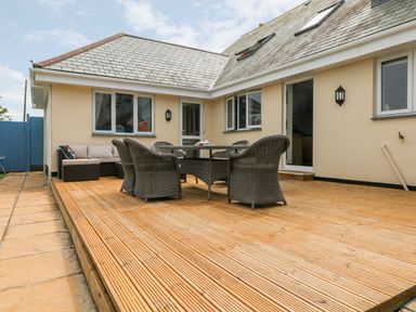 An outdoor patio with wooden decking and wicker furniture at Trevose House in Crantock