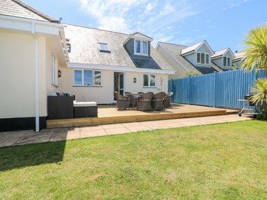 A backyard with a wooden deck patio featuring outdoor furniture and a barbecue grill at Trevose House in Crantock