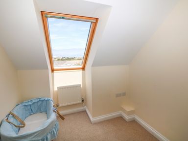 A small room with sloped ceiling a window radiator and a blue baby bassinet at Trevose House in Crantock