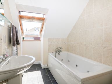 A bathroom with a bathtub a sink a towel rack and a window at Trevose House in Crantock