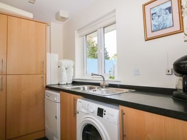 A utility room with a washing machine dishwasher sink and cupboards under a window at Trevose House Crantock