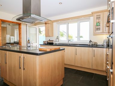 A kitchen with wooden cabinets black countertops an island with a cutting board a bottle of wine and two wine glasses at Trevose House in Crantock