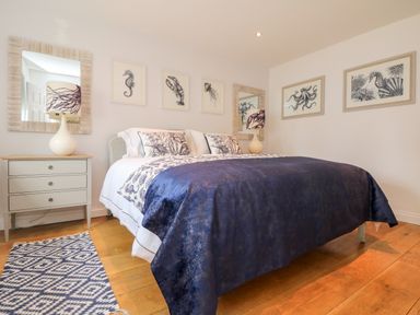 A bedroom with a double bed blue bedspread bedside tables lamps and marine life artwork at Trevose House in Crantock